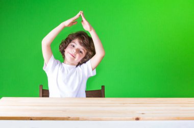 Gülümseyen ve kameraya bakarak baş evini, onun elele kıvırcık sevimli çocuk. Yakın çekim. Yeşil arka plan.