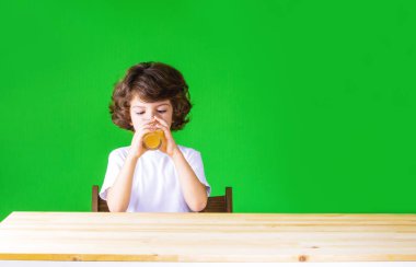 Kıvırcık sevimli çocuk masada oturan cam suyu içer. Yakın çekim. Yeşil arka plan.