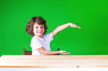 Kameraya bakarak bir masada oturan eller hayali hediye tutarak kıvırcık sevimli çocuk. Yakın çekim. Yeşil arka plan.