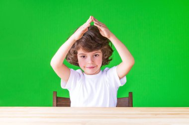 Kameraya başının üzerine bulmak ellerini sıktı evine kıvırcık şirin çocuk. Yakın çekim. Yeşil arka plan.