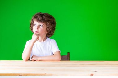 Kıvırcık saçlı güzel çocuk sağ yukarı, oturma bir masada dik dik bakıyor. Yakın çekim. Yeşil arka plan.