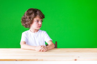 Kıvırcık saçlı yakışıklı masada oturan kuşkuyla sol görünüyor. Yakın çekim. Yeşil arka plan.