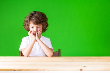 Kıvırcık küskün çocuk elleri kameraya bakarak üzgün yüz dokunmadan. Yakın çekim. Yeşil arka plan.