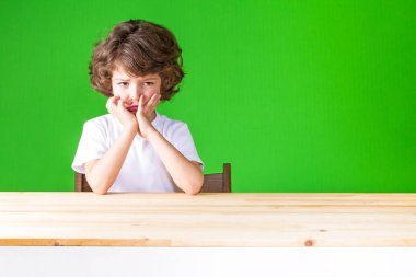 Kıvırcık çocuk elleri kameraya bakarak üzgün yüz dokunmadan. Yakın çekim. Yeşil arka plan.