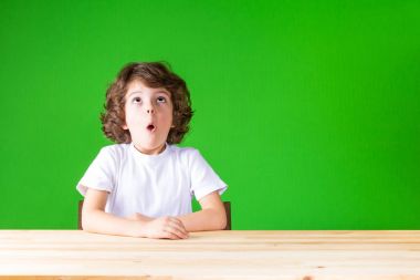 Kıvırcık çocuk yukarı, openmouthed bakar. Yakın çekim. Yeşil arka plan.