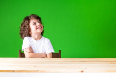 Kollarını ile kıvırcık çocuk gülüyor ve tarafına bakarak geçti. Yakın çekim. Yeşil arka plan.