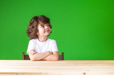 Uzağa arıyorsunuz gülümseyen kıvırcık çocuk kollarını ile geçti. Yakın çekim. Yeşil arka plan.