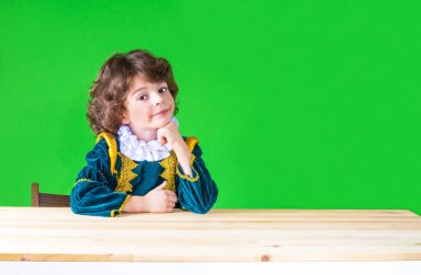 Kıvırcık saçlı yakışıklı prens giysili kameraya bakarak başını yaslanır. Yakın çekim. Yeşil arka plan.