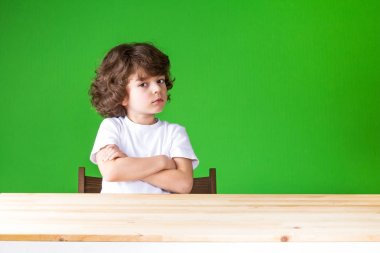 Kollarını ile kıvırcık çocuk ne yazık ki kameraya bakarak geçti. Yakın çekim. Yeşil arka plan.