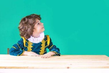 Kıvırcık saçlı yakışıklı prens giysili kafası soldaki tablo üzerinde elini koydu. Yakın çekim. Turkuaz arka plan.