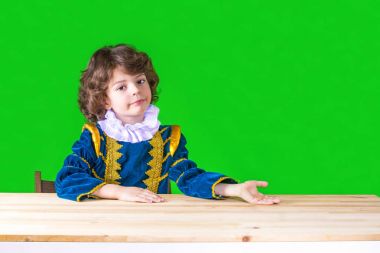 Kameraya bakarak Prens giysili üzgün kıvırcık çocuk. Yakın çekim. Yeşil arka plan.