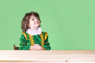 Kıvırcık saçlı yakışıklı prens giysili midesini palms basıldığında arama yapar. Yakın çekim. Yeşil arka plan.