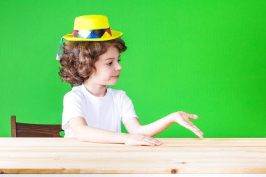 Sarı palyaço şapkalı küçük kıvırcık çocuk ona bakmak kadar onun sağ el palm döndü. Yakın çekim. Yeşil arka plan.