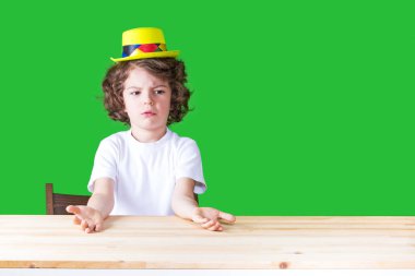 Öfkeyle el hareketi bir sarı palyaço şapkalı küçük kıvırcık çocuk. Yakın çekim. Yeşil arka plan.