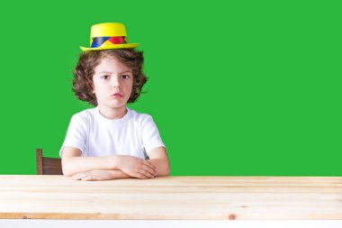 Palyaçonun ağzını açık kameraya bakarak şaşkınlık içinde sarı şapkalı küçük kıvırcık çocuk. Yakın çekim. Yeşil arka plan.