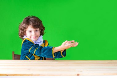 Prensin giyim şirin küçük çocuk iki ellerinde tutan hayali bir nesne kameraya bakarak gülümsüyordu. Yakın çekim. Yeşil arka plan.