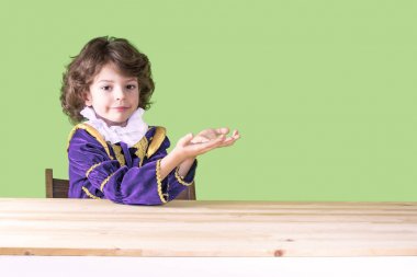 Prens giysileri tutuşup kameraya bakarak bükülmüş hayali konuda gülümseyen sevimli küçük mod. Yakın çekim. Yeşil arka plan.