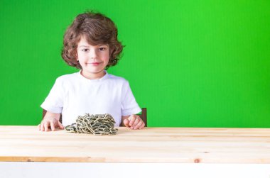 Mutlu küçük Kıvırcık kafalı çocuk Beyaz gömlekli bir masada oturur. Masaya hasas bir zinciridir. Yakın çekim. Yeşil arka plan.