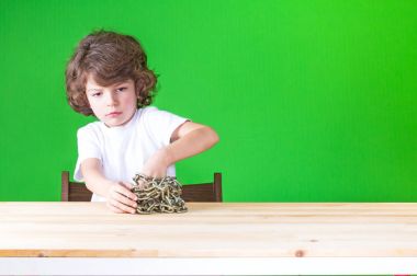 Beyaz bir t-shirt yakışıklı-özgür masada oturan zincirleri, gelen küçük kıvırcık çocuk. Yakın çekim. Yeşil arka plan.