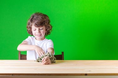 Beyaz bir gömlek küçük kıvırcık çocuk bir masada, eller serbest, bağlı zinciri oturur. Yakın çekim. Yeşil arka plan.