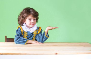 Kameraya bakarak Palm'da hayali nesne tutan gülümseyen şirin Prens giysili küçük mod. Yakın çekim.