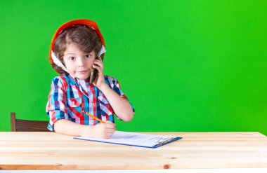 Gülümseyen, kameraya bakarak bir defter kalem yazma bir telefon tutarak küçük kıvırcık foreman. Yakın çekim. Yeşil arka plan.