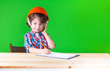 Genç sevimli baş komiser kask kameraya bakarak bir defter kalem yazıları telefonda konuşuyor. Yakın çekim. Yeşil arka plan.