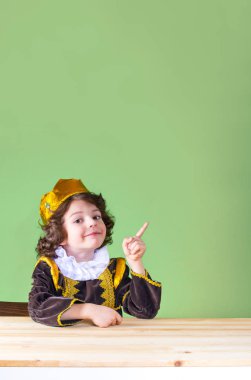 Küçük yakışıklı prens kameraya bakarak, işaret parmağı ile işaret. Yakın çekim. Yeşil arka plan.