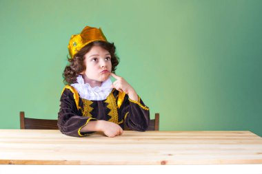 Küçük kıvırcık Kral sert görünmüyor. Mor kıyafet. Yeşil arka plan.