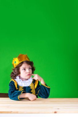 Küçük kıvırcık ararken öfkeyle, Kral. Bir parmak yanağını sıkar yumruk iliştirin. Yeşil arka plan.