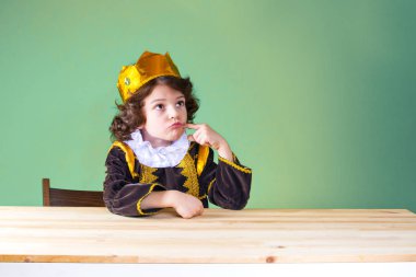 Küçük kıvırcık ararken öfkeyle, Kral. Bir parmak yanağını sıkar yumruk iliştirin. Mor kıyafet. Yeşil arka plan.