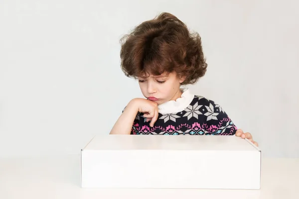 Sorprendido chico lindo buscando triste en una caja blanca. El suéter con adorno. Fondo blanco . — Foto de Stock