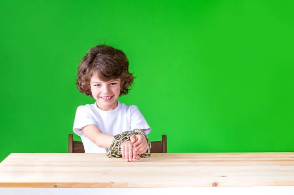 Elleriyle bir zinciri tarafından bağlı kıvırcık çocuk gülüyor ve kamera seyir oturur. Yakın çekim. Yeşil arka plan. — Stok fotoğraf
