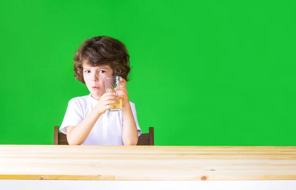 Bir bardak meyve suyu, holding kıvırcık saçlı güzel çocuk kameraya bakıyor. Yakın çekim. Yeşil arka plan. — Stok fotoğraf