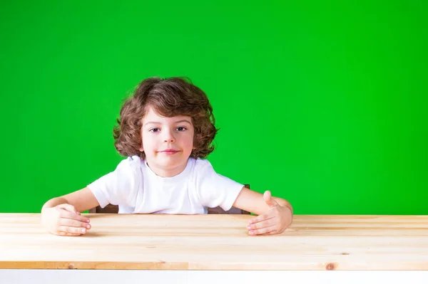 그의 손을 가상 상자 포옹 곱슬 귀여운 소년입니다. 테이블에 앉아 있다. 클로즈업입니다. 녹색 배경. — 스톡 사진
