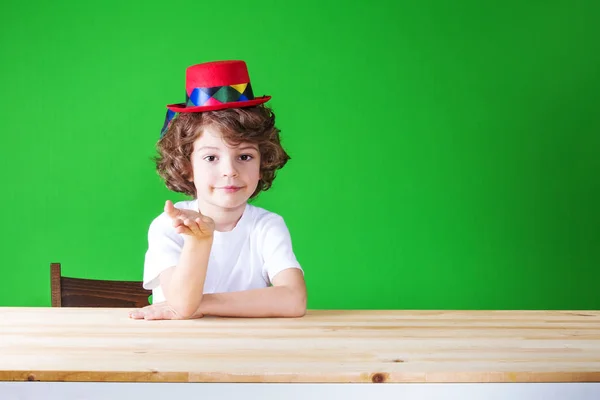 작은 곱슬 소년 광대 모자 귀여운 미소 유지 손에서 상상의 일 카메라 보고 합니다. 클로즈업입니다. 녹색 배경. — 스톡 사진