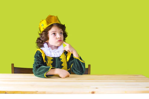 Маленький кудрявый король строго смотрит вверх. Зеленый костюм. Желтый фон . — стоковое фото