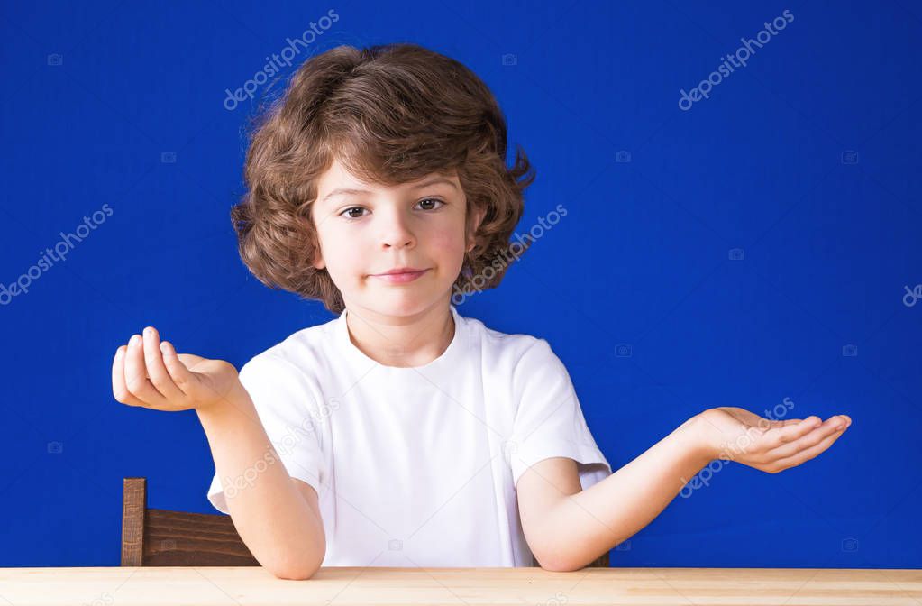 Curly cute boy spread his arms and looking at the camera. Blue background.