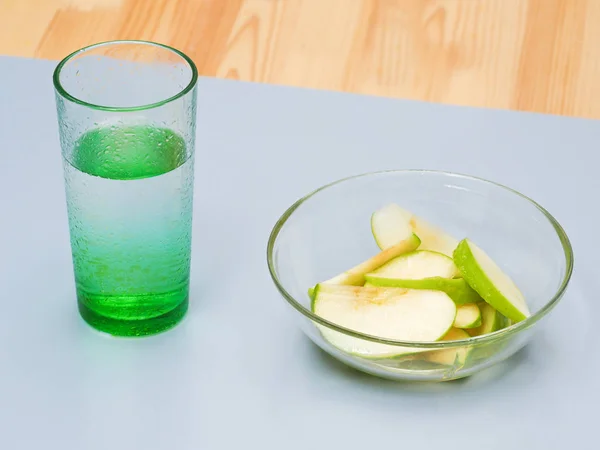 Нарізане зелене яблуко лежить в тарілці з медом. Поруч стоїть склянка води . — стокове фото
