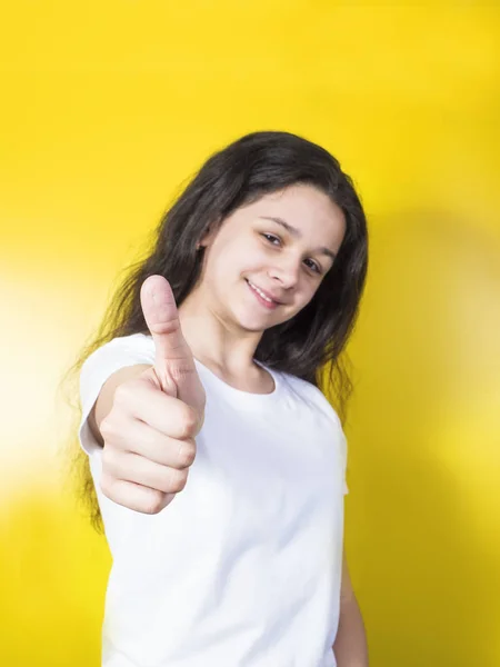 Beautiful young girl smiling extends a hand forward and shows gesture class.Yellow background — Stock Photo, Image