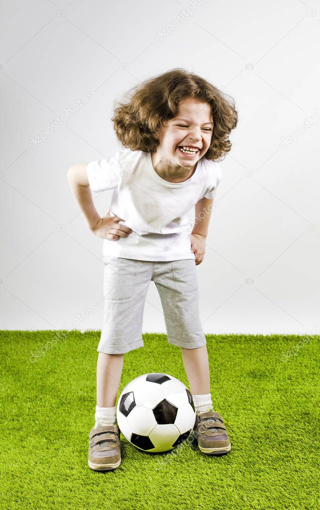 Little boy in white shorts and white shirt playing with a soccer ball. Fun boy laughs out loud.