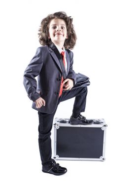 İş takım elbiseli küçük çocuk ayağı siyah bavula koy. Beyaz arka plan