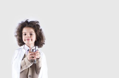 Bir bardak su tutan ve kameraya bakarak şirin küçük kıvırcık saçlı çocuk doktoru. Gri arka planı