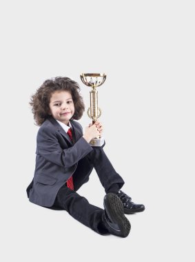 Sevimli küçük kıvırcık çocuk siting ve bir fincan tutan bir takım elbise. Gri arka planı