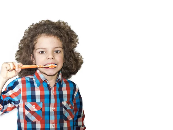 Un petit garçon aux cheveux bouclés se brosse les dents avec une brosse à dents. Fond blanc . — Photo