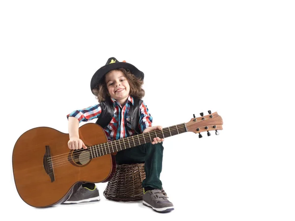검은 모자에 귀여운 소년 기타와 고리 버들 세공 바구니에 앉아 있다. 흰색 배경 — 스톡 사진