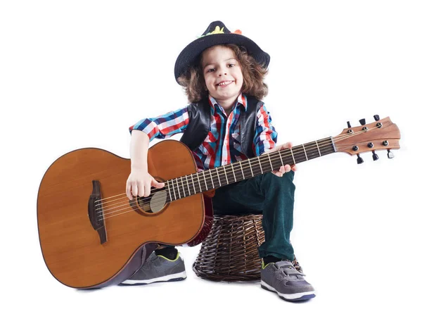 Söt liten pojke i svart hatt sitter på en korg med gitarr. Vit bakgrund — Stockfoto