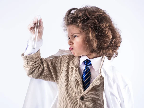 Un niño de pelo rizado ilittle en un vestido médico sostiene un tubo de ensayo con una mano. Fondo blanco . — Foto de Stock