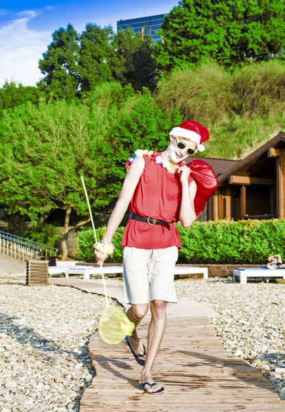 ビーチで新年。サンタ クロースのプレゼントの袋とビーチの上を歩いてします。休日の楽しいコンセプト. — ストック写真