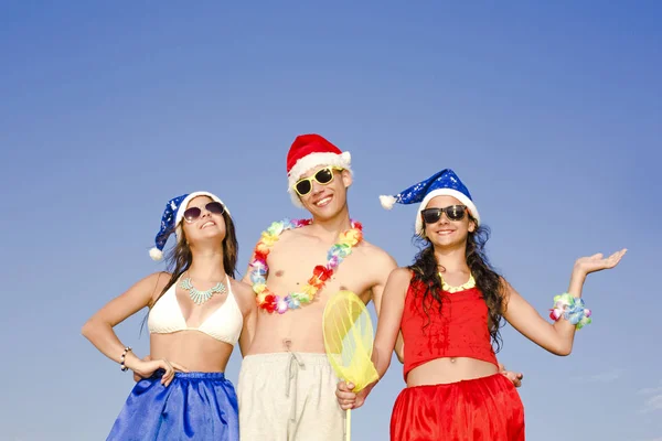 Concepto: Año Nuevo en la playa. La compañía - el muchacho y dos muchachas en la ropa para un nuevo año en la playa —  Fotos de Stock